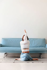 Full length of woman exercising against sofa at home