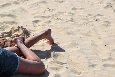 Low section of woman relaxing on sand at beach