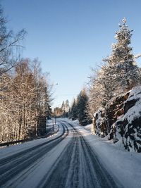 Road amidst trees against clear sky during winter