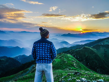 Rear view of man standing on mountain against sky during sunset