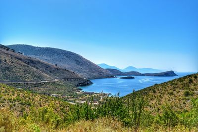 Scenic view of sea and mountains against clear blue sky