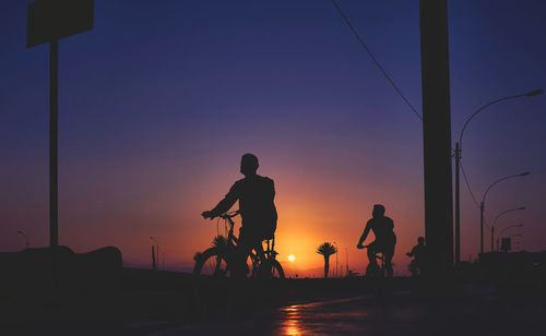 Silhouette people standing on street against sky during sunset