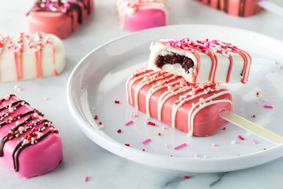 Valentine's day cakesicles on a plate with sprinkles with a bite out of one.