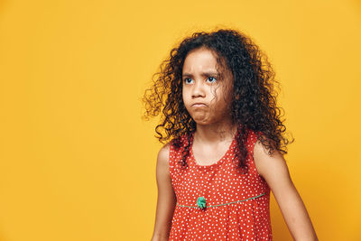 Portrait of young woman standing against yellow background