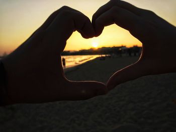 Close-up of hand holding heart shape against sky during sunset