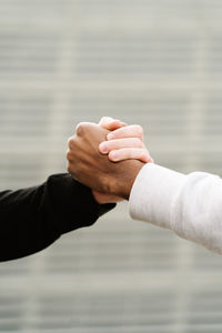 Side view of unrecognizable stylish young diverse male friends in trendy outfits standing on paved street in city and shaking hands