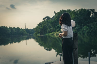 Rear view of woman standing by lake against sky