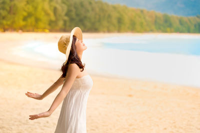 Side view of young woman wearing hat standing at beach