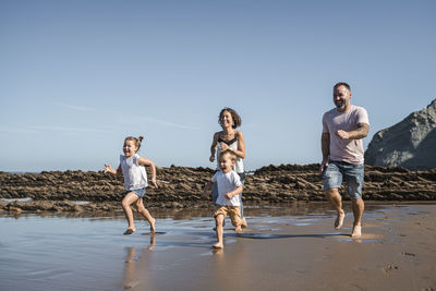 Cheerful family running at beach against sky