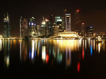 Illuminated buildings by river against sky at night