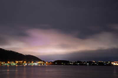 Illuminated city by sea against sky at night