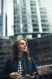 Young woman looking away against buildings in city