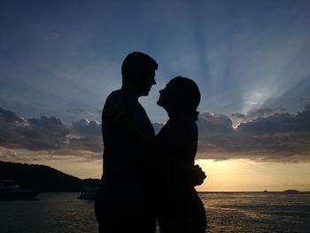 Man and woman standing against sea during sunset