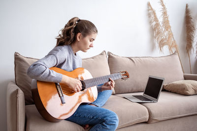 Side view of girl playing guitar at home