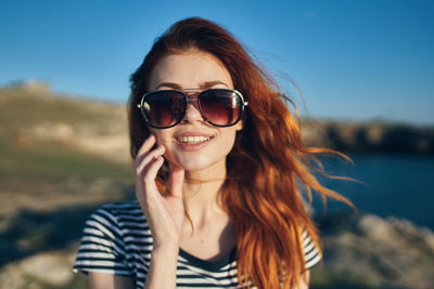 Portrait of smiling young woman wearing sunglasses against sky