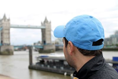 Close-up of man wearing blue cap looking at tower bridge