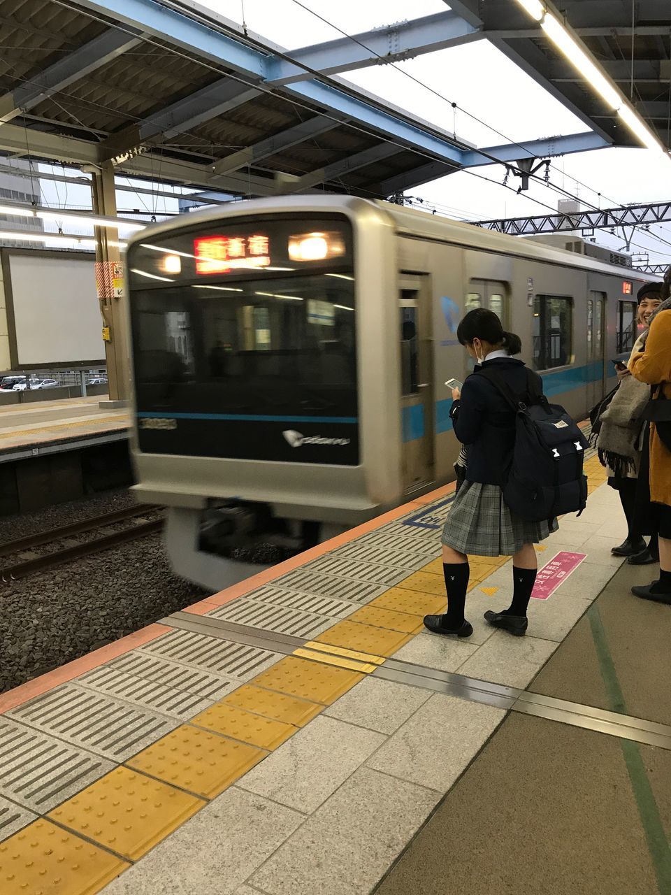 transportation, public transportation, train - vehicle, real people, railroad station platform, mode of transport, rail transportation, one person, passenger train, railroad station, women, lifestyles, standing, rear view, full length, men, travel, railroad track, journey, illuminated, day, outdoors, adult, people