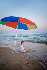 Boy sitting on beach by sea against sky