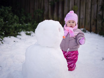 Cute toddler girl standing by snowman during winter