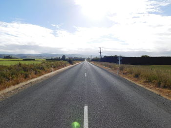 Empty road amidst field against sky