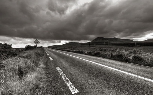 Road passing through field against cloudy sky