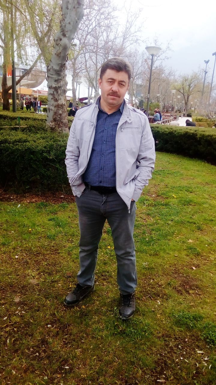 one person, plant, standing, tree, real people, young men, front view, looking at camera, grass, young adult, portrait, full length, land, field, hands in pockets, nature, day, lifestyles, men, outdoors