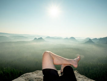Low section of man relaxing on mountain against sky