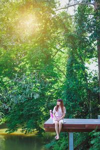 Woman sitting on bench against trees