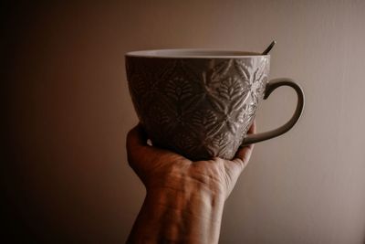 Close-up of hand holding coffee cup against wall