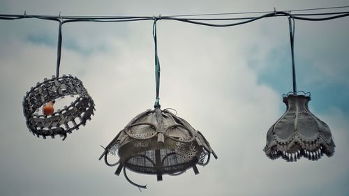 Low angle view of electric lamps hanging against cloudy sky