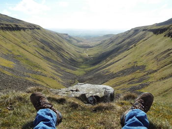 Low section of man sitting on hill against sky