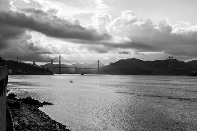 View of suspension bridge over sea against cloudy sky