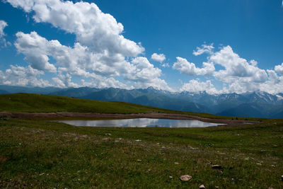 Scenic view of grassy field by lake against sky