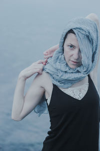 Woman covering face with scarf while standing by sea