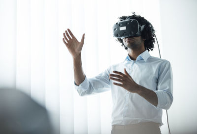 Young businessman wearing virtual reality headset while gesturing in board room at office