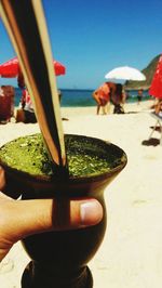 Close-up of hand holding drink at beach