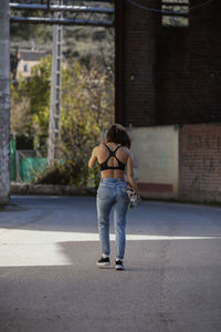 Rear view full length of young woman walking with skateboard on street