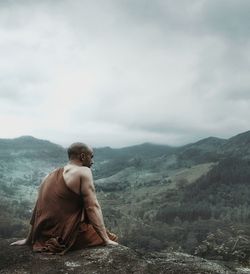 Man sitting on mountain against sky