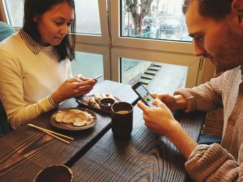 Young woman using smart phone while sitting on table