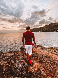 Rear view of man standing on beach against sky during sunset