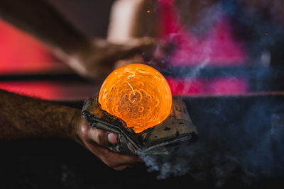 Close-up of cropped hand holding molten glass in factory