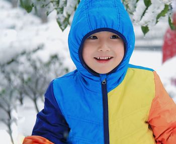 Close-up of smiling boy wearing hooded jacket in snow