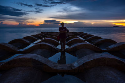 Man on sea against sky during sunset