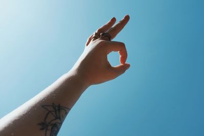 Low angle view of woman hand against clear blue sky
