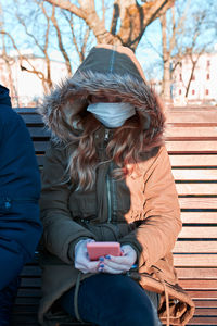 Teenage girl wearing mask while using mobile phone