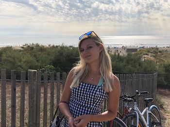 Portrait of young woman with bicycle on railing against sea