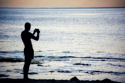 Silhouette man standing at beach against sky