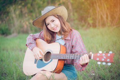 Young woman playing guitar on grassy field at park