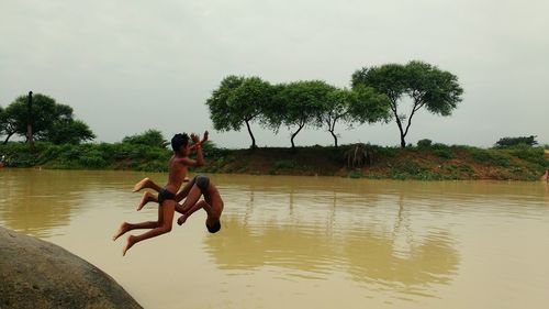 Shirtless young men jumping into lake