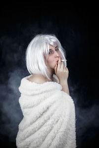 Portrait of female model smoking cigarette against black background